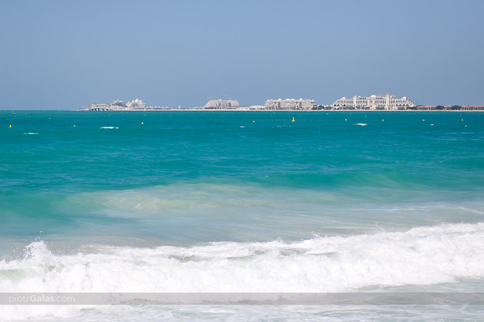 Dubaj 2013 // Widok na Palm Jumeirah z pobliskiej plaży Jumeirah Beach Residence, popularnie określanej skrótem JBR. Palm Jumeirah Island, bo tak brzmi pełna nazwa, to legendarna wyspa palma, zbudowana od podstaw przez człowieka na otwartych wodach Zatoki Perskiej. Palma, tak jak i Dubai Marina, powstały z bardzo błachego powodu. Włodarze Dubaju uznali, że do rozwoju atrakcyjnej mieszkaniowo tkanki miejskiej potrzeba lini brzegowej, nad którą będzie można budować mieszkania marzeń. Był przy tym tylko jeden problem - Dubaj jest płaski i praktycznie powstał na pustyni, więc ciężko było o odpowiednio ciekawą linię brzegową powstałą w sposób naturalny. Jeśli jej nie było, to trzeba było ją zbudować i tak właśnie zrodziły się te projekty, dzięki którym za mieszkania w tym rejonie można wydać kosmiczne pieniądze.